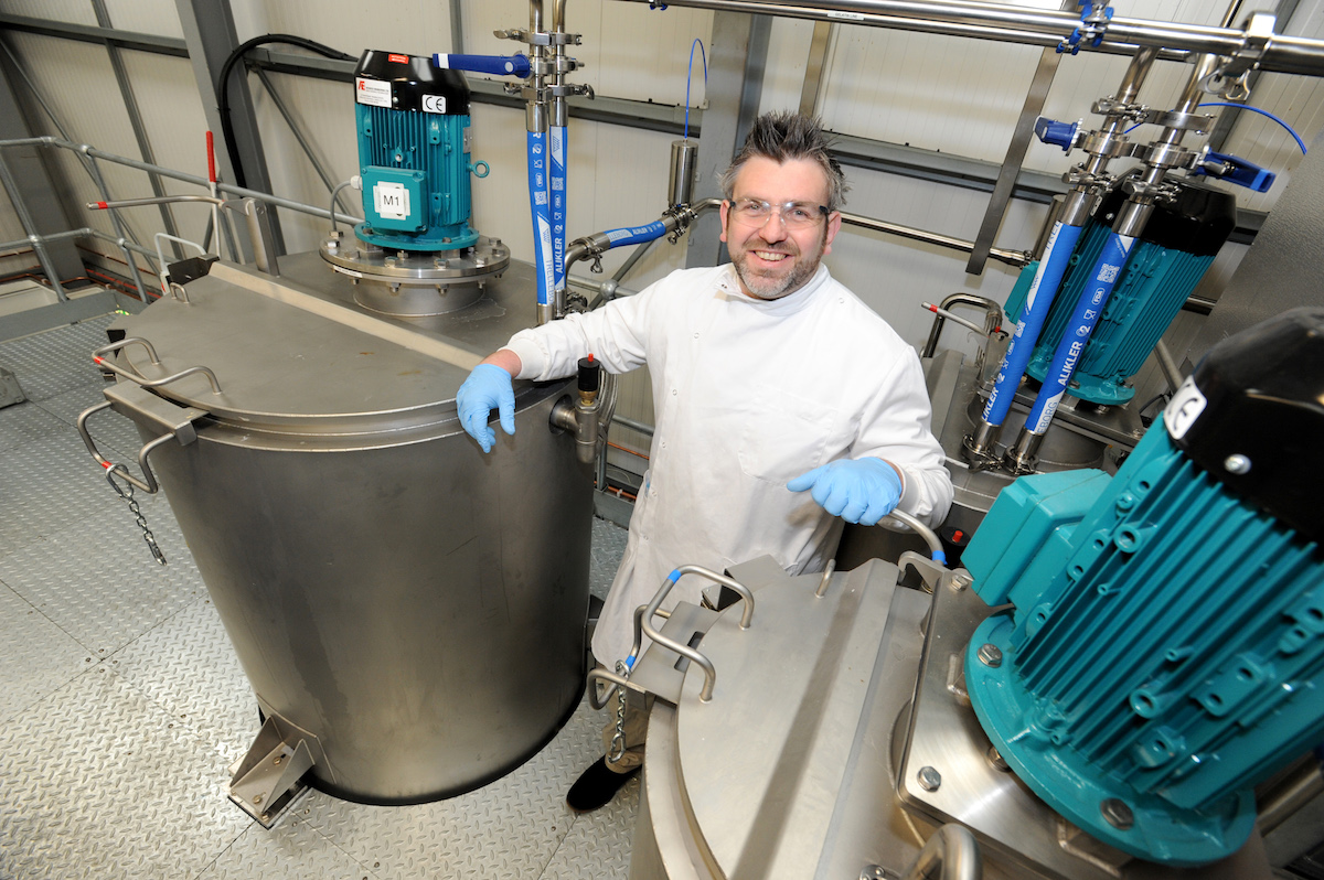 Man in laboratory coat and PPE standing next to machinery