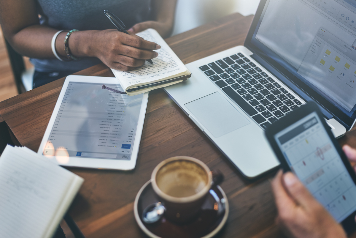 3 people sat around a coffee table using a laptop, tablet and mobile phone