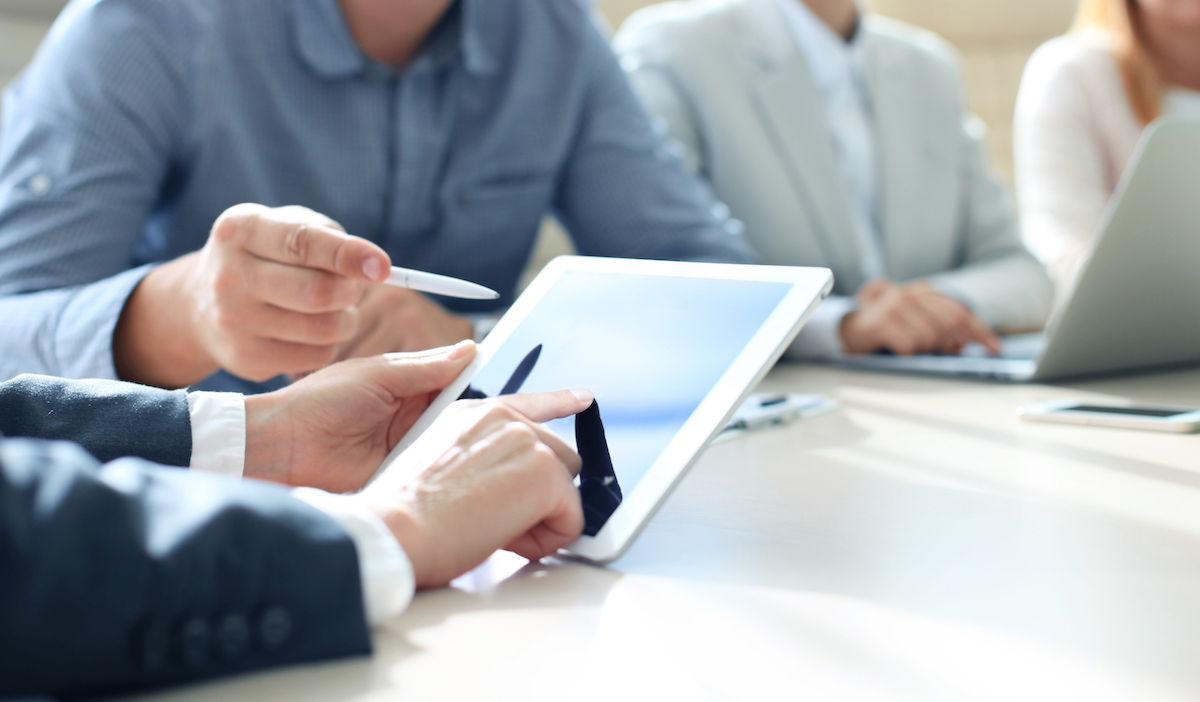 Hands typing on a mobile tablet device whilst in a meeting