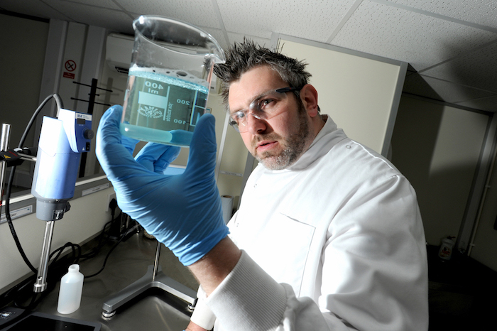 Man in laboratory environment looking at liquid in a jar
