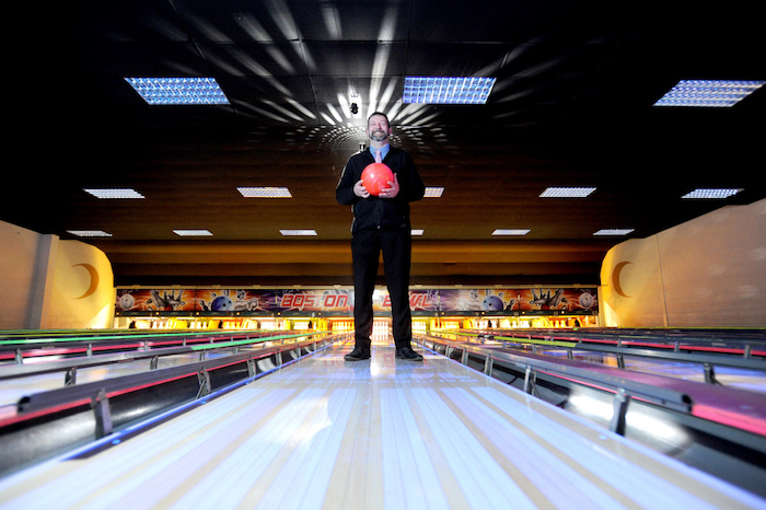 Man stood in a bowling lane holding a red bowling ball