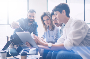 4 people sat working together on a laptop and tablet device