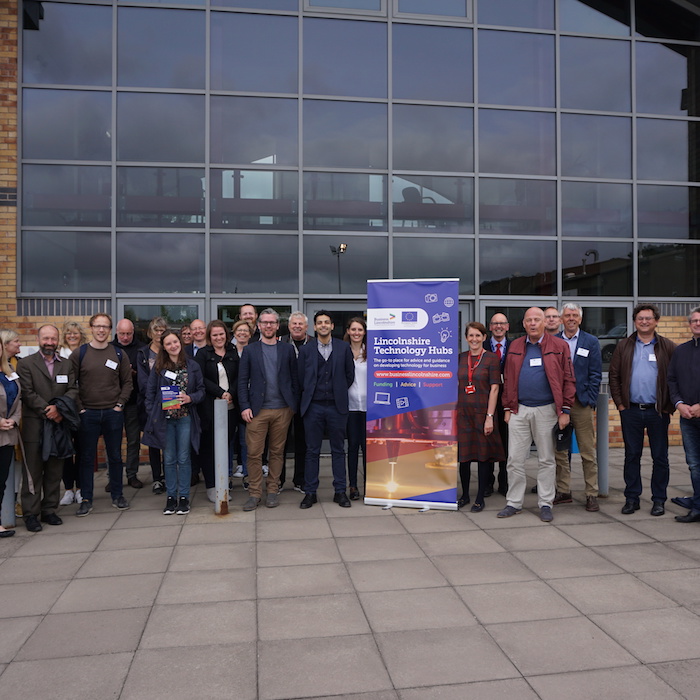 Large group of people stood next to Lincolnshire technology hub sign in front of building