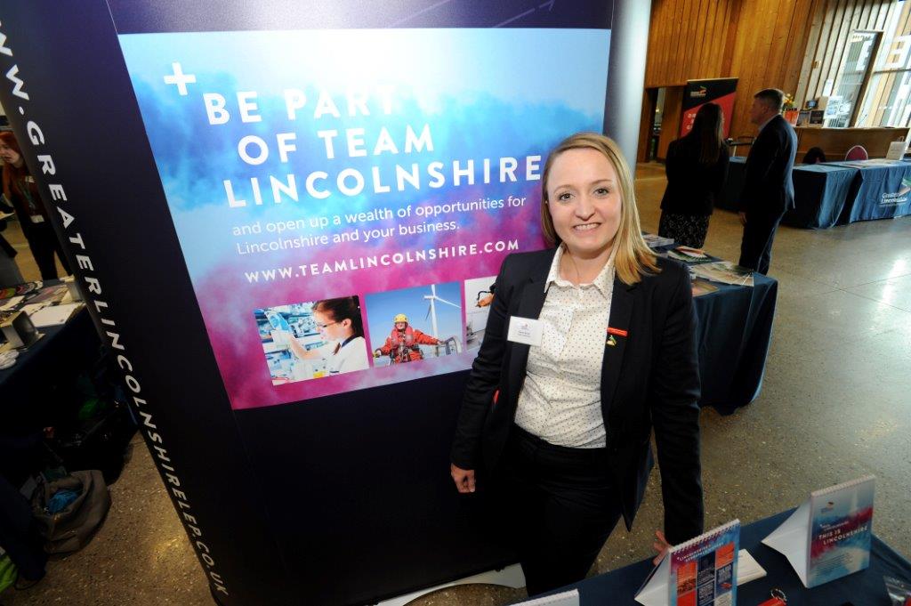 Lady smartly dressed stood in front of event poster