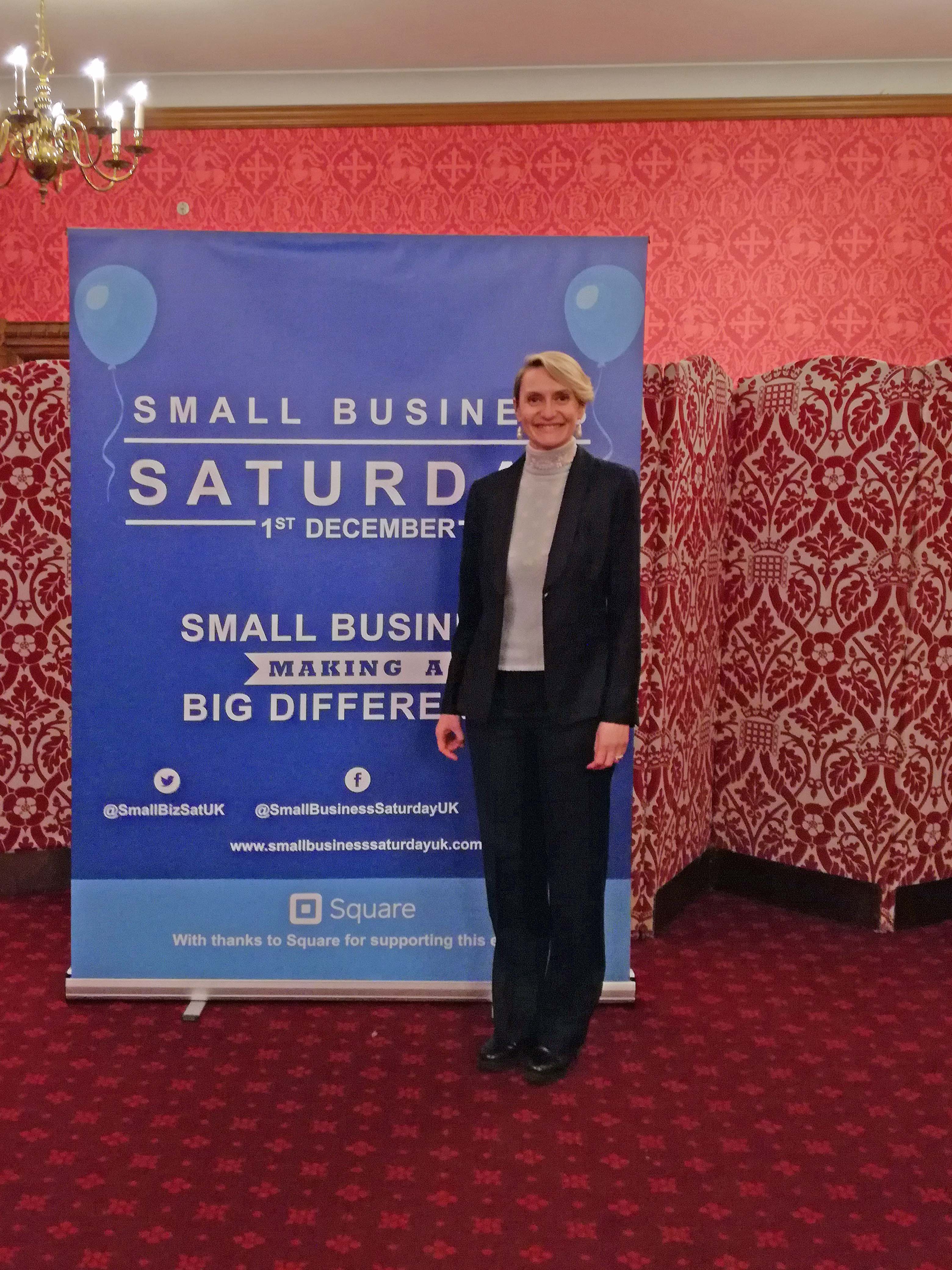 Lady smartly dressed stood in front of event poster
