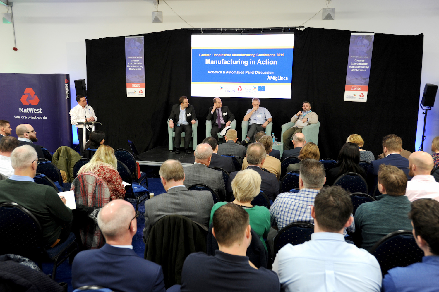 Large group of people sat down at an event listening to a Manufacturing Panel presentation