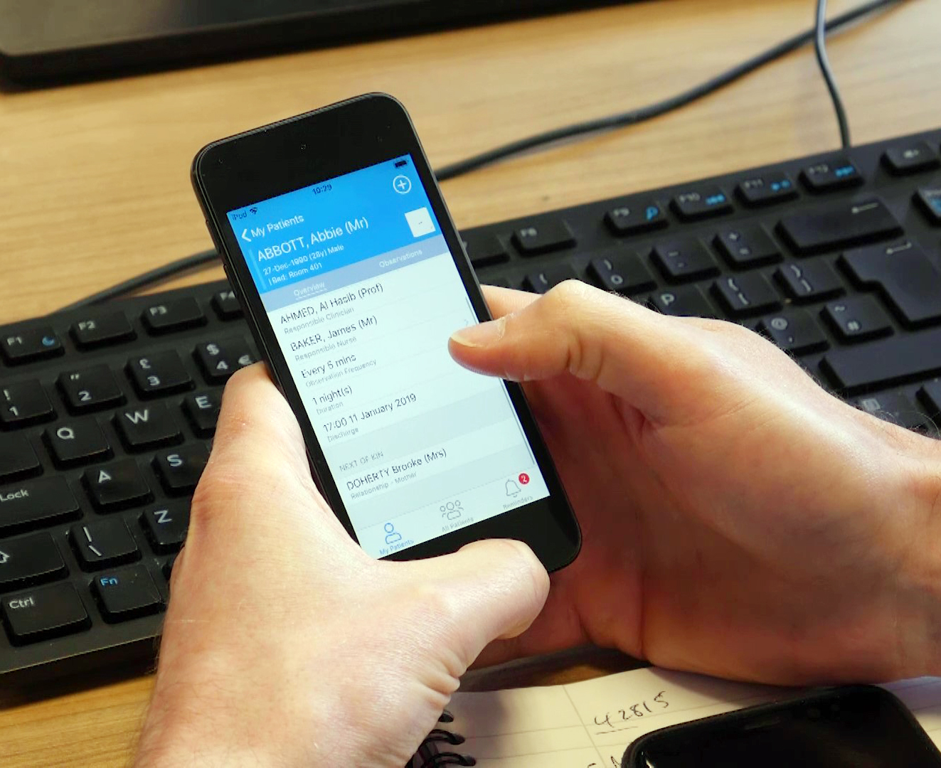 Hand holding a mobile phone with contact details showing, keyboard in the background