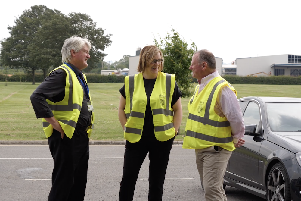 2 men and 1 lady all wearing Hi Vis vests stood next to a car talking