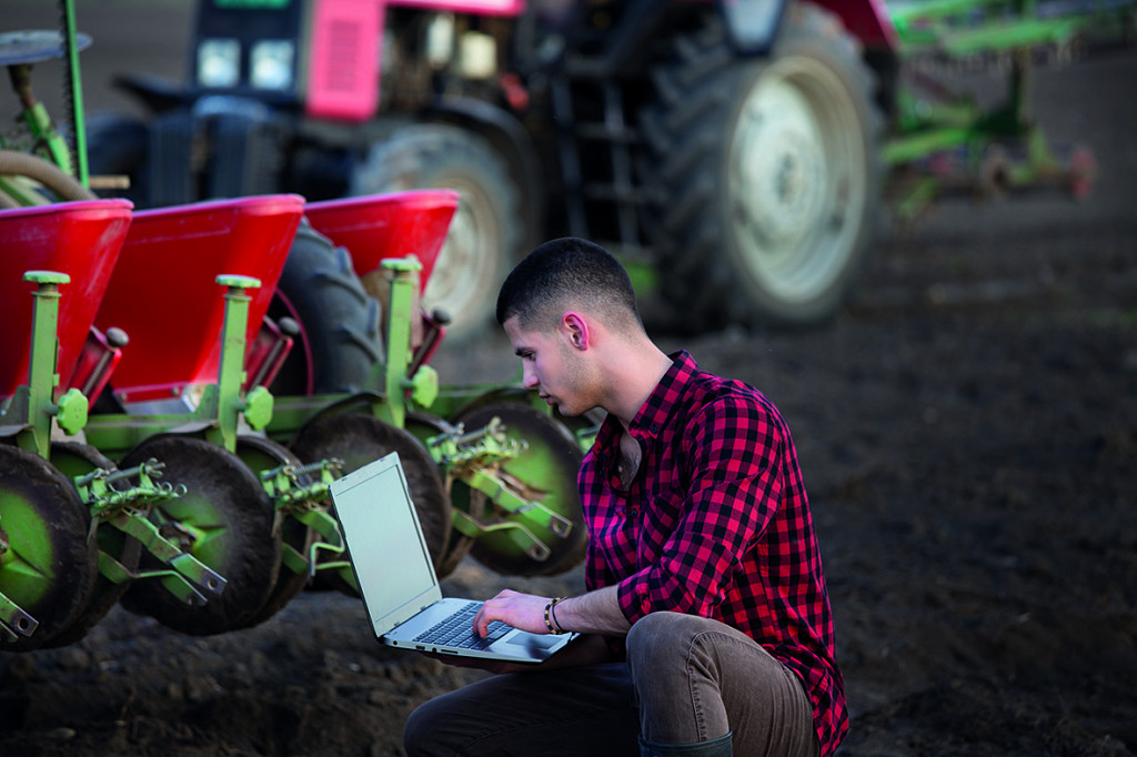 Man working on laptop in front of farming equipment