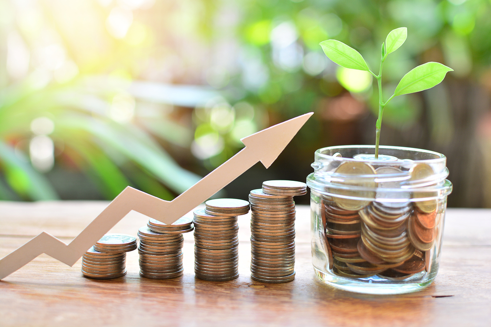 Coins stacked in piles with arrow ascending upwards above them with a glass pot filled with coins with a plant growing from the top