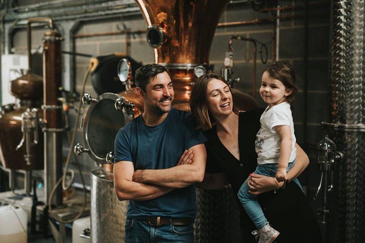 Family image of man, lady and young child stood in front of distilling equipment
