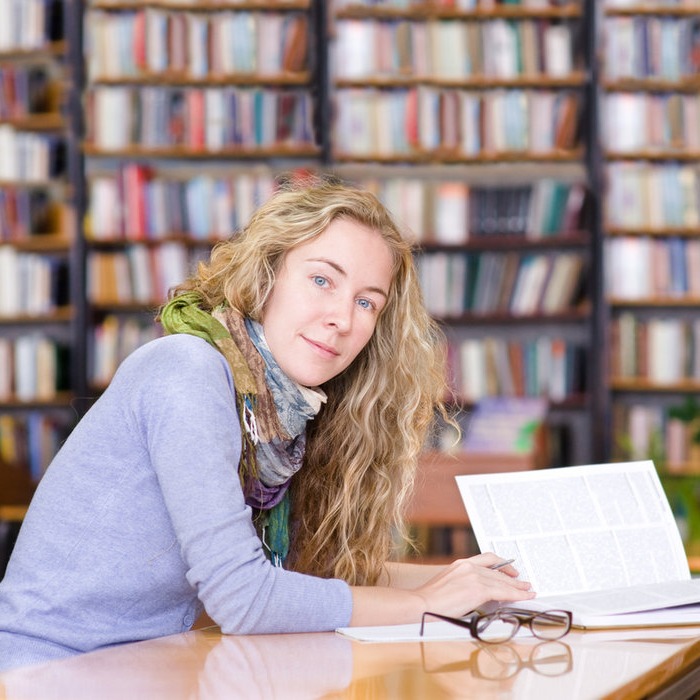 Lady reading book sat at desk in front of bookshelf