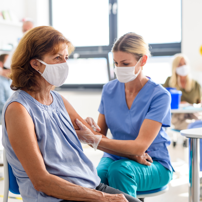 Older  brunette woman being vaccinated by a young blonde nurse