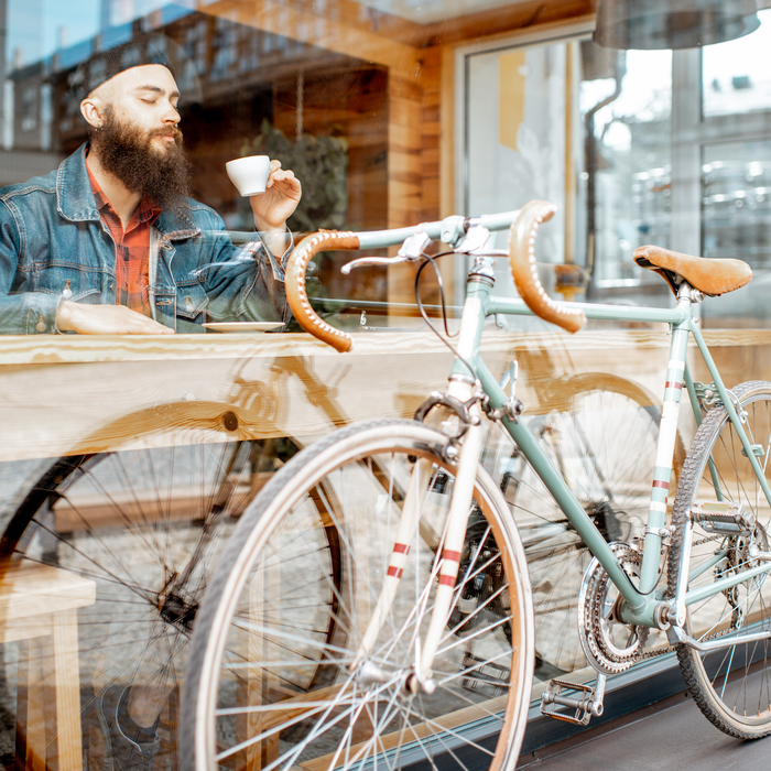 Man with beard sat inside cafe looking out onto bike. 