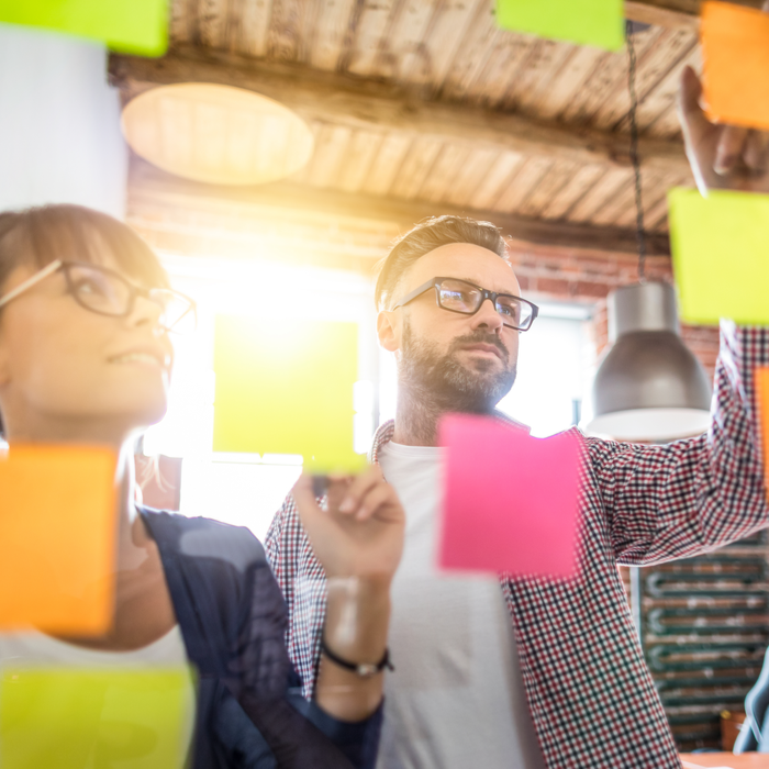 2 people looking at coloured post it notes on a glass board