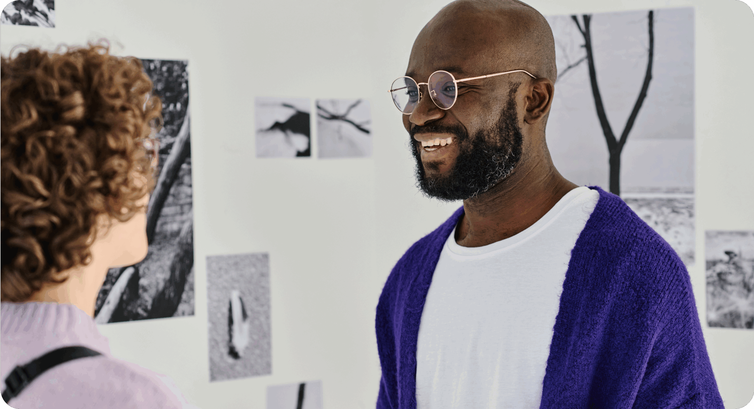 A man with glasses on talking to a lady with artwork and photography pictures in the background