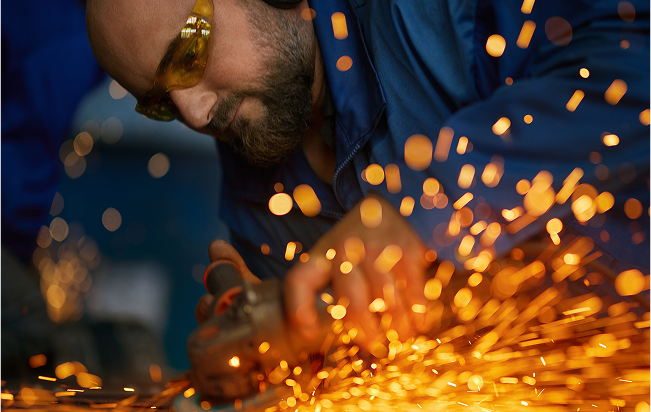 A man with blue overalls on and orange safety googles using a tool which had orange sparks flying everywhere - manufacturing and engineering - Business Lincolnshire